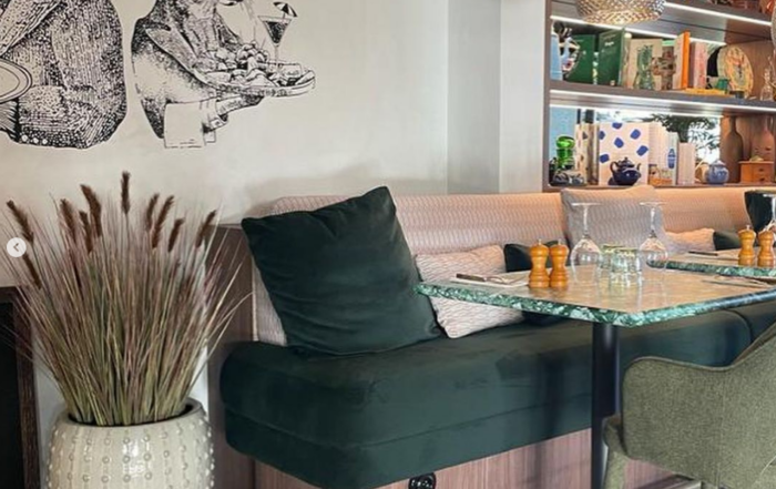 Intérieur de restaurant moderne avec décoration murale d'animaux humanisés, banquettes rose pâle, coussins verts, table en marbre, et étagères décorées